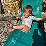 toddler, child, outdoor, sunlight, chair, sandals, stone_wall, garden_gnomes, playful, smiling, summer, relaxing, striped_shirt, legs, hand, shadow, gravel, green_chair, portrait, daytime