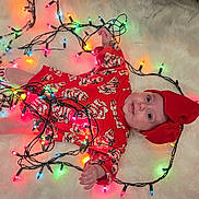 Nylah is registered to the contest to win money with this photo: baby, child, christmas_lights, red_clothing, headband, bow, festive, holiday, smiling, lying_down, white_fur, socks, cute, indoors, holiday_season, playful, colorful_lights, infant, toddler, portrait