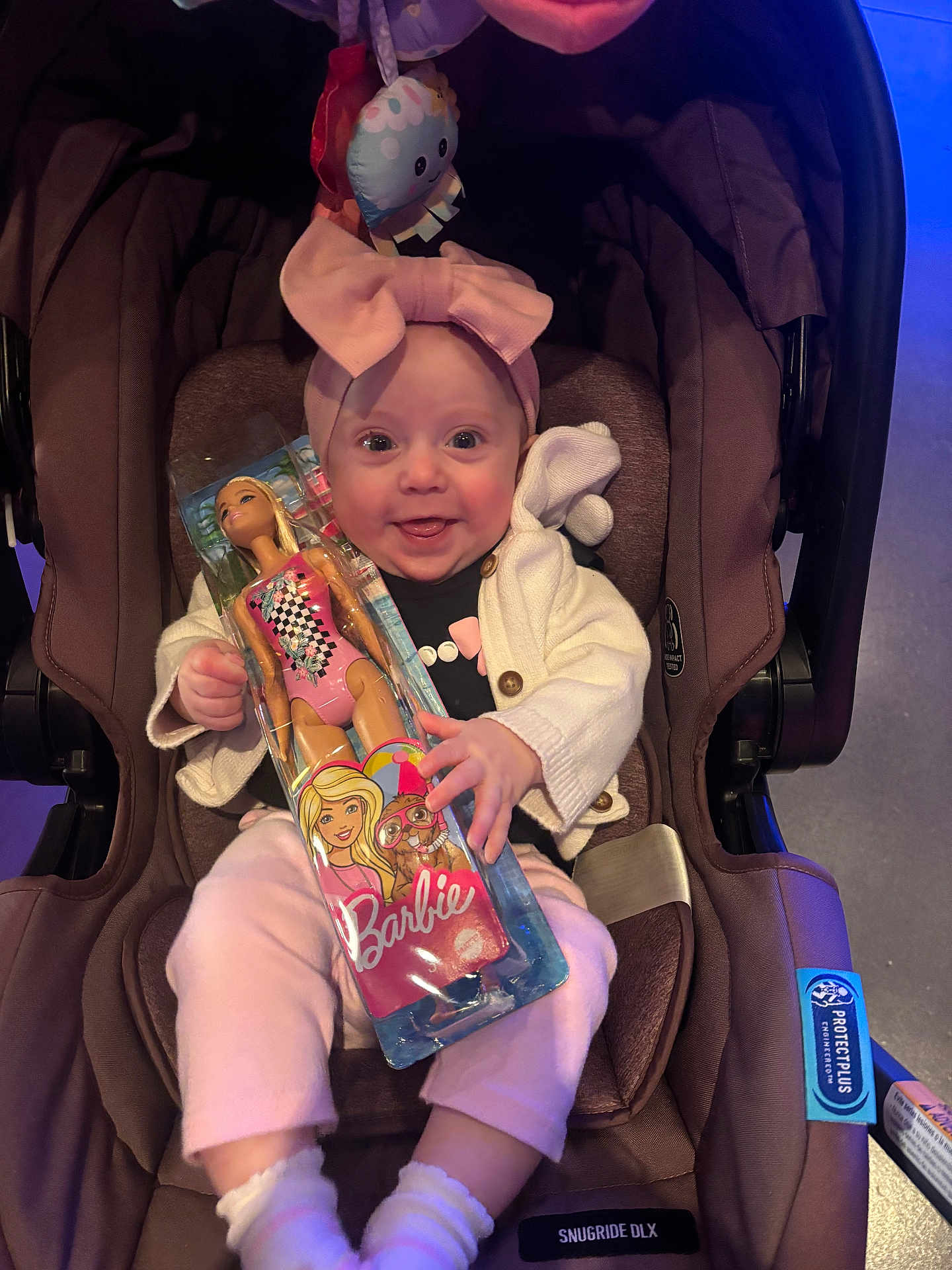 Nylah is registered to the contest to win money with this photo: baby, car_seat, barbie_doll, toy, pink_clothing, headband, smiling, child, infant, happy, indoor, seat, young_child, cute, playful, packaging, person, portrait, clothing, accessory