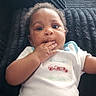 Deandre joined the competition — help win amazing prizes! baby, infant, child, portrait, sitting, sofa, couch, onesie, clothing, hand, fingers, smiling, curious, indoors, living_room, furniture, dark_background, photography, face, timestamp