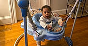 Deandre joined the competition — help win amazing prizes! baby, infant, child, activity_jumper, toy, sitting, indoors, wooden_floor, home, playroom, colorful, curious, portrait, face, eyes, clothing, furniture, door, shelf, social_media_screenshot
