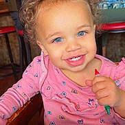 Paisley joined the competition — help win amazing prizes! toddler, child, baby, smiling, happy, curly_hair, blue_eyes, pink_shirt, floral_pattern, thumbs_up, high_chair, restaurant, table, activity_book, toy, indoor, portrait, face, seated, colorful