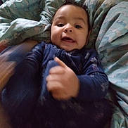 Ezekiel is registered to the contest to win money with this photo: baby, child, infant, blue_clothing, blanket, bed, smiling, face, hand_motion, indoor, cute, young, person, portrait, cozy, soft_texture, happy, lying_down, warm, playful