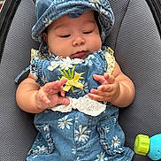 Evangeline joined the competition — help win amazing prizes! baby, child, infant, blue_clothing, hat, floral_pattern, cute, hands, toy, gray_background, seated, closeup, adorable, chubby_cheeks, curious, playful, fabric, texture, casual, portrait