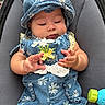 baby, child, infant, blue_clothing, hat, floral_pattern, cute, hands, toy, gray_background, seated, closeup, adorable, chubby_cheeks, curious, playful, fabric, texture, casual, portrait