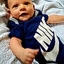 Diego a rejoint le concours — aidez-le/la à gagner de superbes lots ! apparel, baby, blue, child, clothing, cute, fabric, face, hand, happy, infant, laying, nike, onesie, person, smiling, soft, text, towel, white