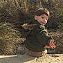 child, boy, outdoor, nature, green_jacket, smiling, rock, trees, bushes, autumn, playful, young, person, casual_clothing, daylight, forest, happy, sitting, landscape, scenic