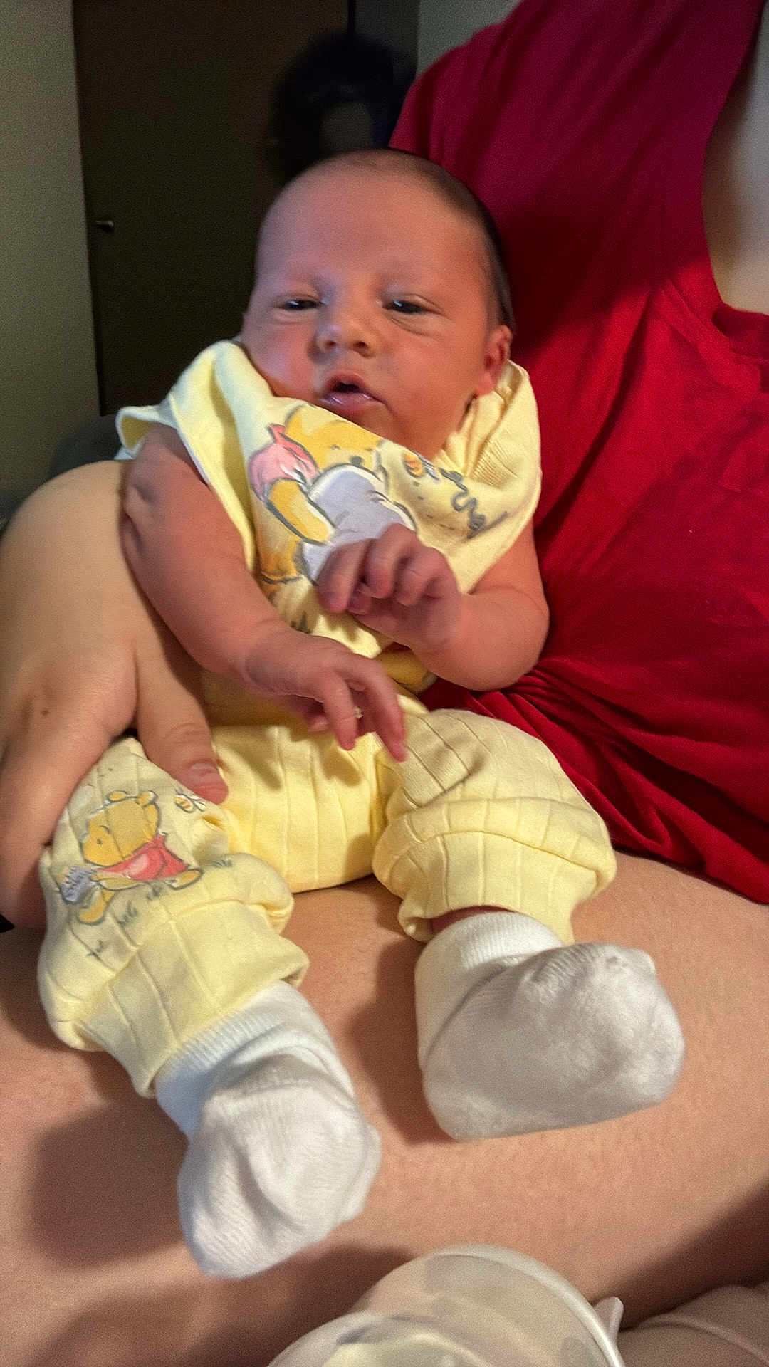 Katalyn is registered to the contest to win money with this photo: baby, infant, newborn, person, lap, yellow_clothing, socks, hand, arm, red_shirt, bottle, portrait, indoor, winnie_the_pooh, cozy, sitting, newborn_clothes, tiny_feet, skin, family_moment