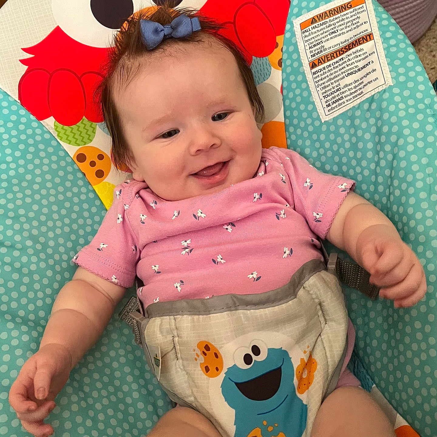 Braelyne is registered to the contest to win money with this photo: baby, baby_seat, blue_cookie_monster, bow, cartoon_characters, child, colorful, cute, fabric, face, happy, indoors, infant, pattern, person, pink_clothing, playful, red_character, seat, smiling
