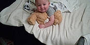 Onyx is registered to the contest to win money with this photo: baby, infant, teddy_bear, bed, blanket, pillow, wall, hanging_plants, leaves, smile, face, indoor, bedding, cozy, child, plush_toy, arm, head, floor, diaper_box