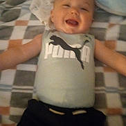 Onyx joined the competition — help win amazing prizes! baby, infant, smiling, onesie, puma_logo, logo, blanket, patterned_blanket, bed, pillow, lying_down, cute, happy, portrait, clothing, arms_out, timestamp, indoor, soft_focus, toddler