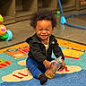 toddler, child, smiling, sippy_cup, play_mat, indoor, toy, colorful, happy, cute, black_jacket, blue_pants, sock, hair, floor, play_area, baby, person, expression, seated