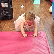 Victoria is registered to the contest to win money with this photo: toddler, child, pink_dress, curly_hair, crawling, pink_mat, playroom, toy, slide, floor, wooden_floor, chair, ball, colorful, indoor, person, baby, curiosity, hands, candid