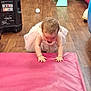 toddler, child, pink_dress, curly_hair, crawling, pink_mat, playroom, toy, slide, floor, wooden_floor, chair, ball, colorful, indoor, person, baby, curiosity, hands, candid