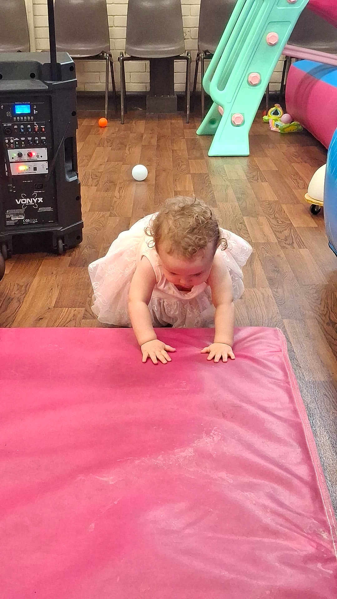 Victoria is registered to the contest to win money with this photo: toddler, child, pink_dress, curly_hair, crawling, pink_mat, playroom, toy, slide, floor, wooden_floor, chair, ball, colorful, indoor, person, baby, curiosity, hands, candid