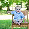 baby, child, blue_eyes, smiling, wooden_chair, outdoor, grass, greenery, shorts, shirt, person, sitting, happy, young_child, sunlight, nature, park, cute, portrait, summer