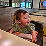 baby, background, blanket, casual, child, face, green_clothing, hair, happy, high_chair, indoor, infant, light, person, restaurant, seat, smile, table, window, yellow_chair