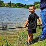 child, boy, fishing, lake, water, grass, fishing_rod, outdoor, nature, smile, person, blue_sky, clouds, shorts, black_tshirt, shoes, adult, summer, greenery, recreation