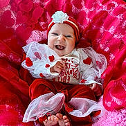 Genevieve joined the competition — help win amazing prizes! baby, smiling, infant, red_clothing, white_clothing, headband, flower_accessory, blanket, pink_blanket, red_blanket, happy, cute, tulle, feet, sitting, indoors, portrait, celebration, heart_pattern, child