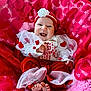 baby, smiling, infant, red_clothing, white_clothing, headband, flower_accessory, blanket, pink_blanket, red_blanket, happy, cute, tulle, feet, sitting, indoors, portrait, celebration, heart_pattern, child