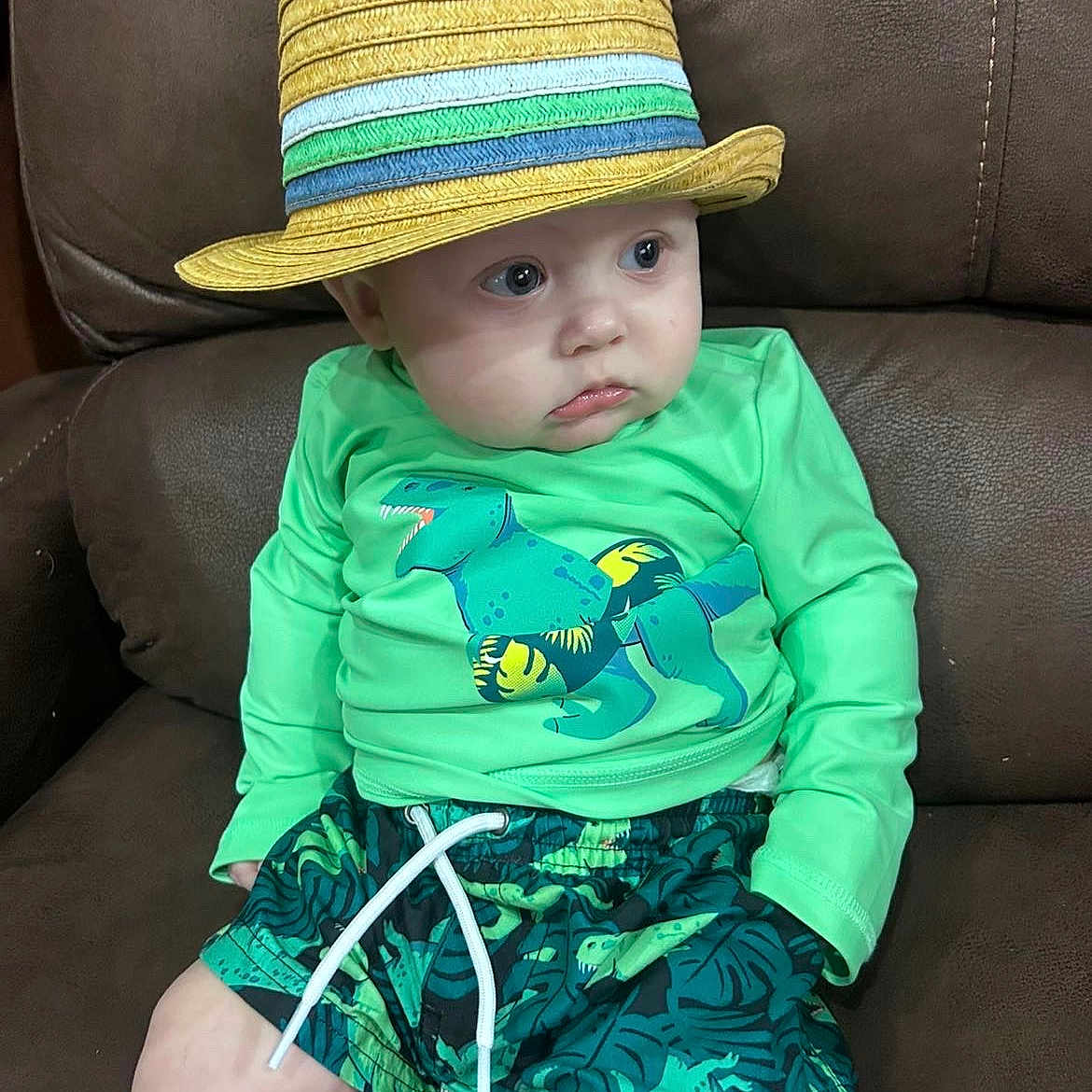 Xavier is registered to the contest to win money with this photo: baby, casual, child, clothing, comfortable, couch, cute, dinosaur_print, expression, green_shirt, hat, indoor, leather, looking_away, person, portrait, shorts, sitting, straw_hat, toddler