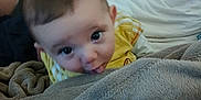 Derek a rejoint le concours — aidez-le/la à gagner de superbes lots ! baby, child, blanket, yellow_clothing, indoor, person, face, tongue, curious, soft_texture, adult_arm, camera, couch, pillow, home, closeup, infant, playful, expression, resting