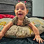 baby, smiling, pigtails, pink_hair_ties, animal_print_clothing, pillow, animal_print_pillow, bedroom, wooden_headboard, baby_hands, happy, cute, child, infant, indoors, face, person, wall, bed, joyful
