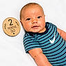 Kolsen is registered to the contest to win money with this photo: baby, infant, child, portrait, smiling, happy, lying_down, striped_shirt, blue_clothing, wooden_sign, milestone, two_months, indoors, white_background, close_up, face, eyes, short_hair, photography, safe