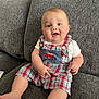 Kalvin joined the competition — help win amazing prizes! baby, child, smiling, sitting, plaid_clothing, romper, red_car_patch, couch, gray_couch, happy, cute, indoors, portrait, infant, young_child, cheerful, person, casual, comfortable, home