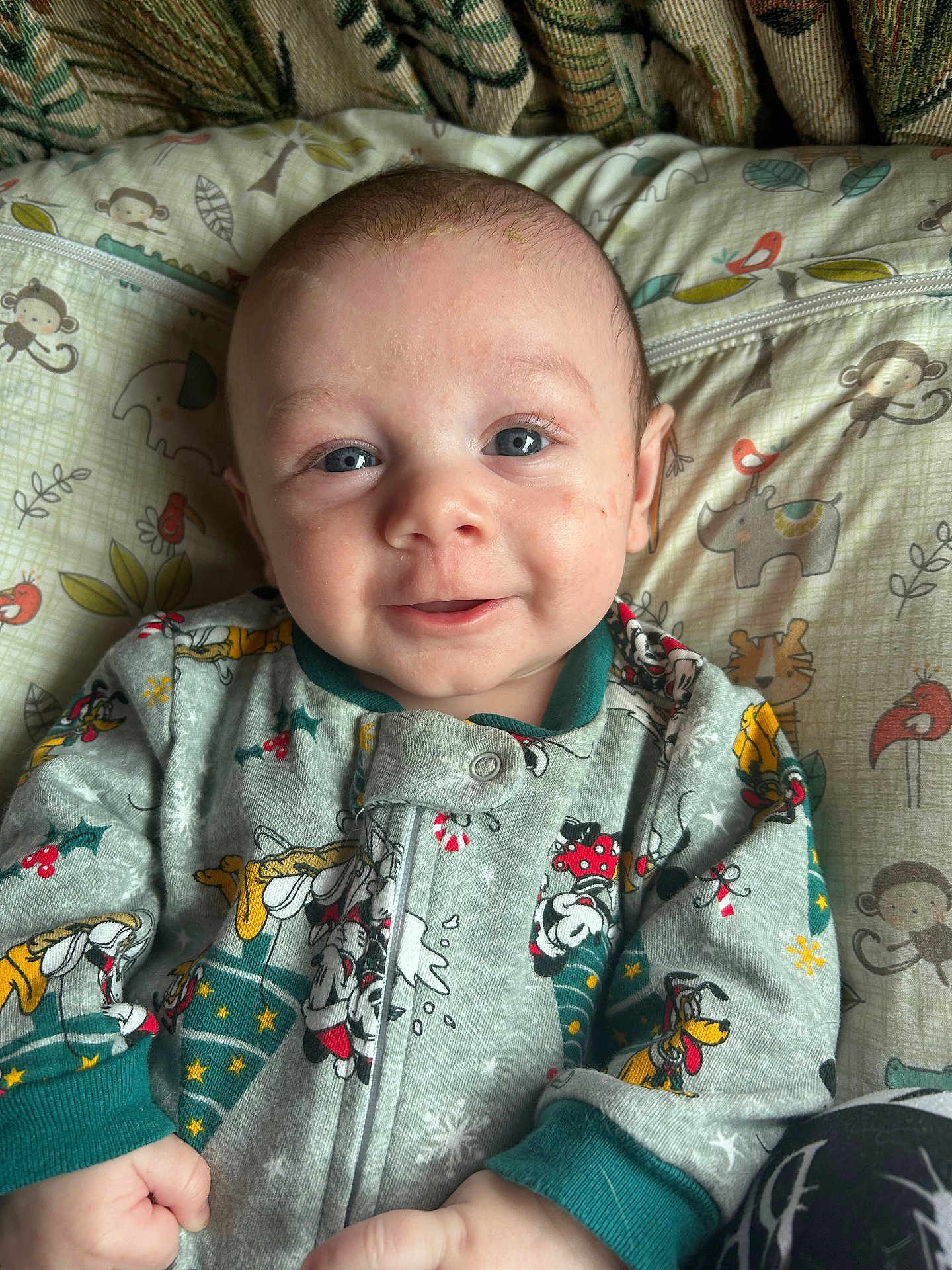 Theodore is registered to the contest to win money with this photo: baby, child, face, smile, pajamas, blue_eyes, infant, cute, lying_down, blanket, pillow, animal_print, monkey, elephant, rhino, tiger, bird, home, cozy, portrait