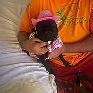 Luna joined the competition — help win amazing prizes! animal, bed, blanket, casual, costume, cute, dog, holding, home, human_hand, indoor, man, orange_shirt, pet, pet_clothing, pink_hat, pink_outfit, pug, red_shorts, resting
