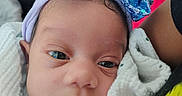 Kalayah is registered to the contest to win money with this photo: newborn, baby, infant, child, face, portrait, close_up, looking_at_camera, eyes, nose, mouth, headband, blue_bow, sequins, blanket, wrapped, clothing, indoors, cuddling, photography