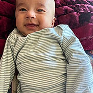 Zakariya is registered to the contest to win money with this photo: baby, blanket, child, closeup, cozy, cute, face, happy, indoors, infant, long_sleeves, person, portrait, red_blanket, sitting, smiling, soft_lighting, striped_clothing, texture, young