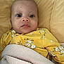 baby, infant, yellow_clothing, floral_pattern, blanket, knitted, cushion, resting, portrait, face, eyes, expression, soft_texture, indoors, child, young, person, cozy, cute, sleepwear