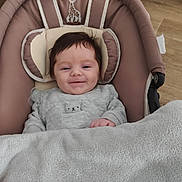 Emma participe au concours pour gagner de l'argent avec cette photo : baby, infant, smile, blanket, pacifier, baby_seat, clothing, bear_design, face, head_support, indoors, floor, wood_floor, cozy, cute, child, portrait, happy, soft, toddler