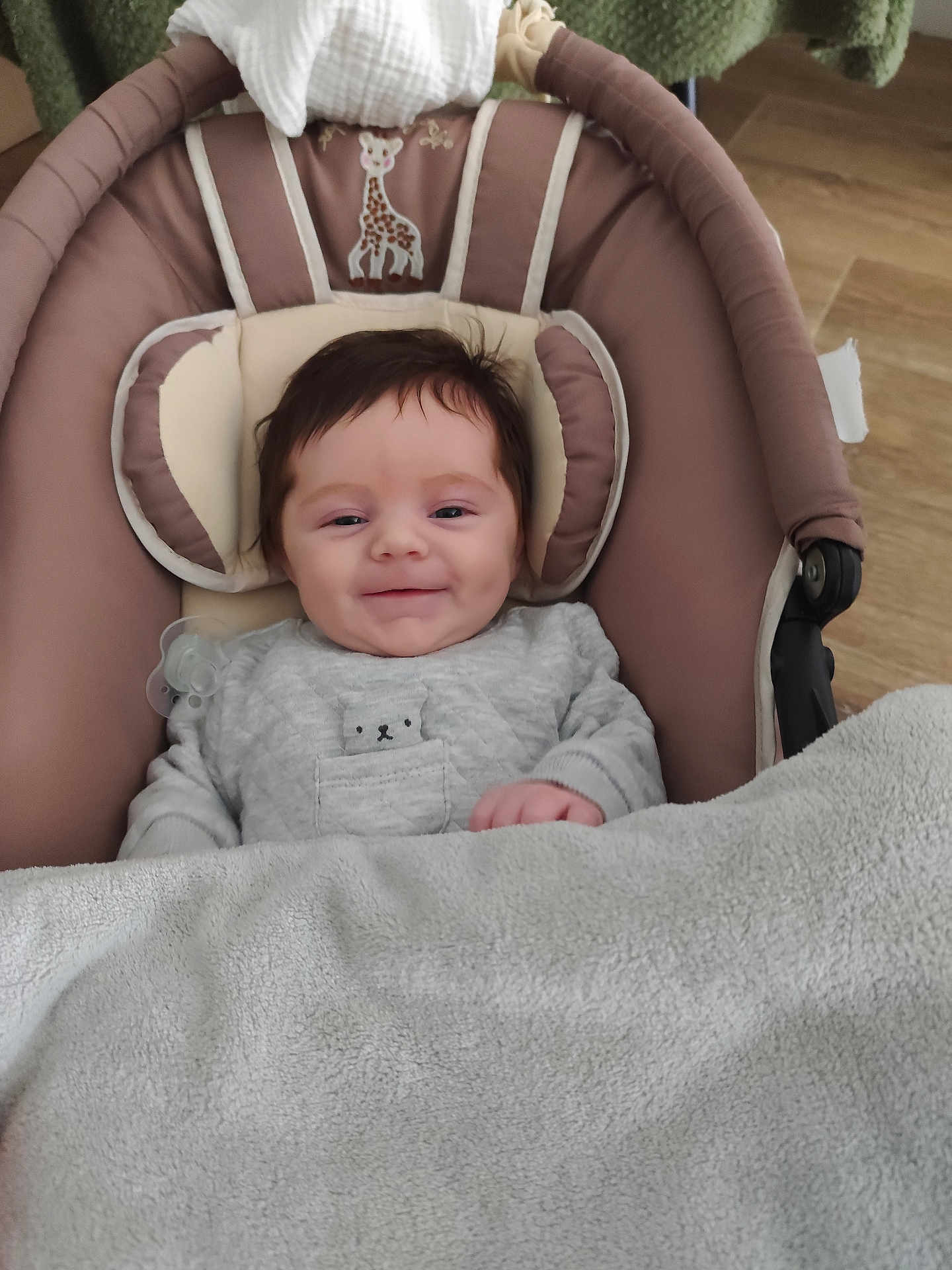 Emma participe au concours pour gagner de l'argent avec cette photo : baby, infant, smile, blanket, pacifier, baby_seat, clothing, bear_design, face, head_support, indoors, floor, wood_floor, cozy, cute, child, portrait, happy, soft, toddler
