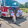 Phoebe joined the competition — help win amazing prizes! fire_truck, children, adult, outdoor, daylight, asphalt, park, trees, casual_clothing, group, smiling, shorts, tshirt, glasses, shoes, sidewalk, shadow, blue_sky, clouds, public_safety