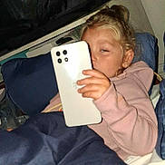 Phoebe joined the competition — help win amazing prizes! bed, blanket, casual, child, clothing, cozy, curly_hair, earrings, face, hand, indoor, nighttime, person, pillow, relaxed, sleepy, smartphone, technology, young