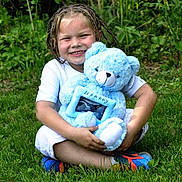 Josiah is registered to the contest to win money with this photo: blue_teddy_bear, braided_hair, child, childhood, cute, daylight, grass, greenery, happy, nature, outdoor, person, playful, portrait, sitting, smiling, sneakers, stuffed_animal, toy, white_clothing