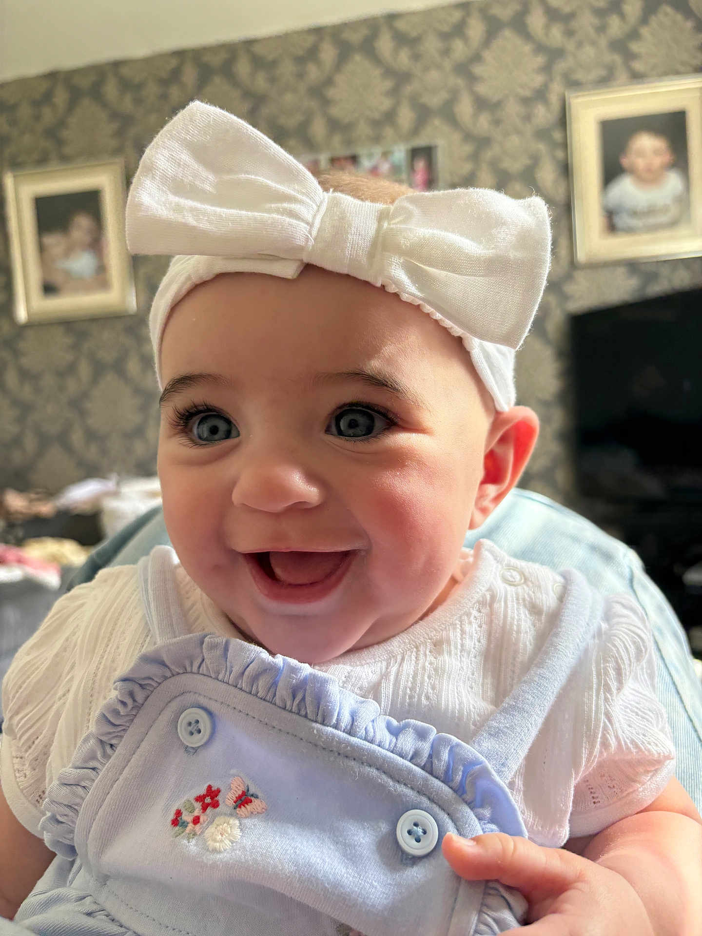 Hazel joined the competition — help win amazing prizes! baby, child, headband, bow, smile, blue_eyes, clothing, overalls, embroidered, hand, portrait, indoor, wallpaper, picture_frame, furniture, happy, cute, person, face, infant
