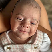 Hazel is registered to the contest to win money with this photo: baby, smiling, close_up, infant, child, face, plaid, clothing, person, soft_lighting, happy, cute, skin, portrait, newborn, resting, lap, warm_tone, button, fabric