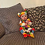 Hazel joined the competition — help win amazing prizes! baby, child, colorful_clothing, hat, striped_couch, pillow, patterned_pillow, sitting, indoor, expression, cute, infant, portrait, cozy, furniture, fabric, happy, person, small, home