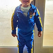 William joined the competition — help win amazing prizes! child, toddler, smiling, blue_tracksuit, yellow_stripes, cartoon_patches, sneakers, standing, indoor, glass_door, doormat, happy, casual_clothing, person, floor_tiles, short_hair, full_body, daylight, home, front_door