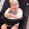 adorable_expression, baby, baby_seat, beige_outfit, bouncer, chubby_cheeks, ergobaby, flower_headband, hands, hardwood_floor, headband, infant, legs, leopard_print, power_cord, rug, seat_strap, smiling, socks, warning_label