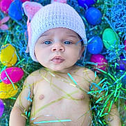 Nylah joined the competition — help win amazing prizes! baby, infant, blue_eyes, knitted_hat, easter_eggs, colorful, decorative_strands, cute, portrait, child, spring, holiday, festive, soft_lighting, closeup, skin, hand, laying_down, headwear, playful