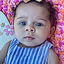 Nylah is registered to the contest to win money with this photo: baby, blue_eyes, bow, curly_hair, striped_clothing, pink_blanket, orange_blanket, flower_decoration, close_up, portrait, infant, child, cute, face, skin, person, head, indoors, soft_texture, colorful_background