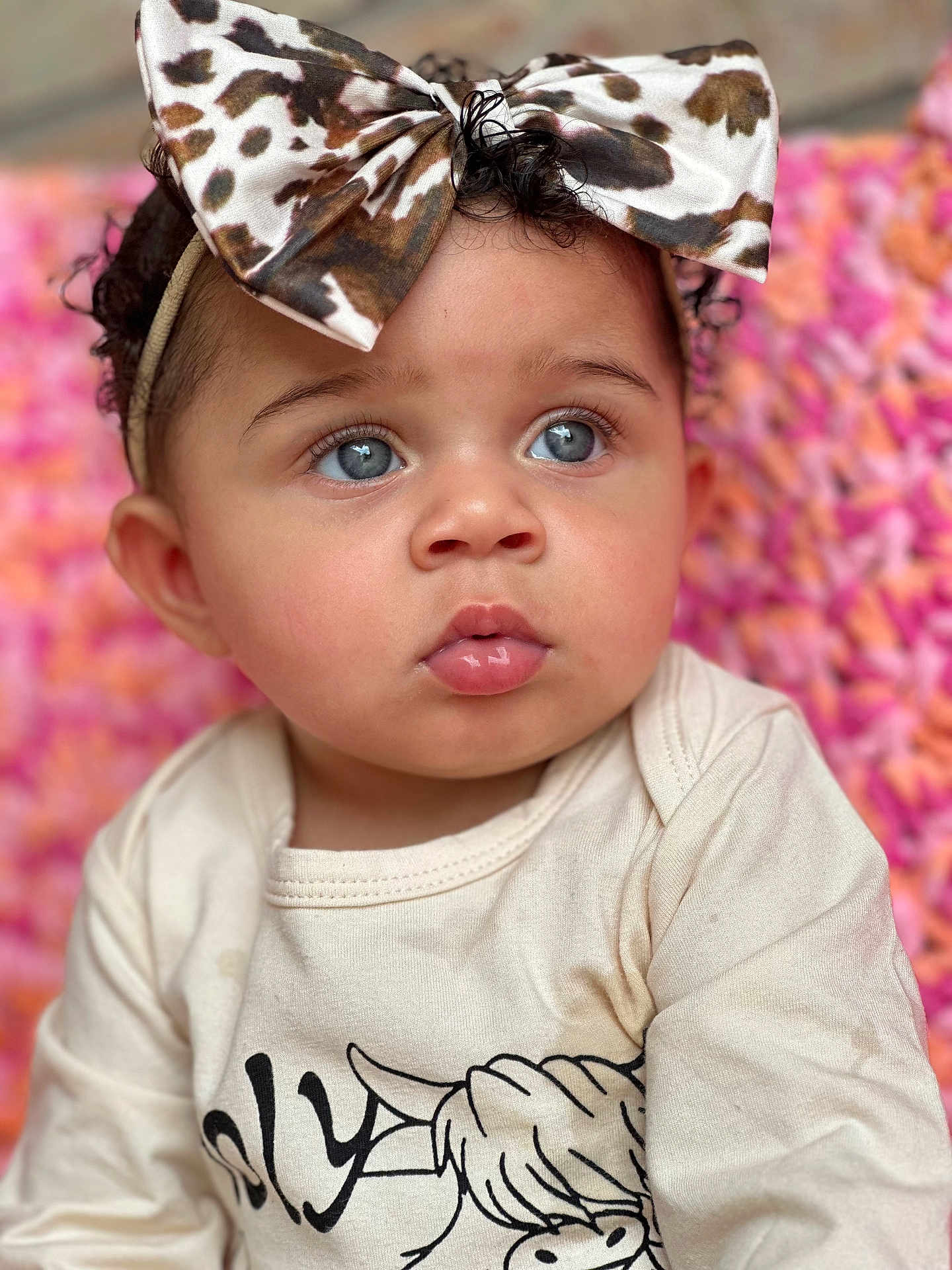 Nylah is registered to the contest to win money with this photo: baby, child, portrait, close_up, blue_eyes, headband, bow, leopard_print, curly_hair, cute, infant, wearing_clothes, pink_background, orange_background, soft_lighting, expression, looking_away, indoor, person, fashion