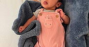 Thalia joined the competition — help win amazing prizes! baby, infant, blanket, pink_overalls, bassinet, face, tongue_out, curious_expression, blue_blanket, safety_instructions, newborn, baby_clothing, cozy, indoor, child, person, soft_texture, head, cute, resting