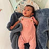 baby, infant, blanket, pink_overalls, bassinet, face, tongue_out, curious_expression, blue_blanket, safety_instructions, newborn, baby_clothing, cozy, indoor, child, person, soft_texture, head, cute, resting