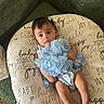 baby, infant, cushion, blue_clothing, bow, face, person, lying_down, furniture, sofa, text, pattern, home_interior, carpet, cute, child, smile, small_hands, legs, resting
